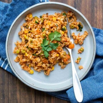 Grey plate on a wooden table filled with Mexican rice and topped with cilantro