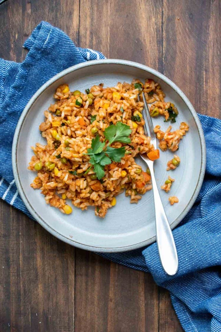 Grey plate on a wooden table filled with Mexican rice and topped with cilantro