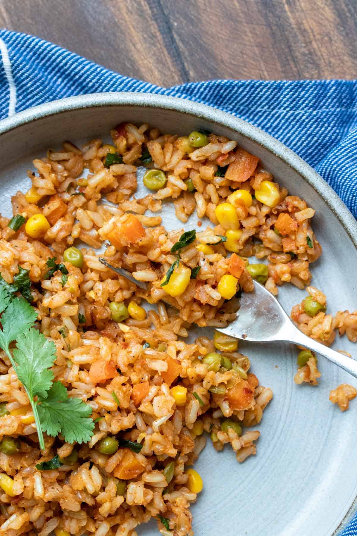 A fork getting a bite of Mexican rice from a grey plate