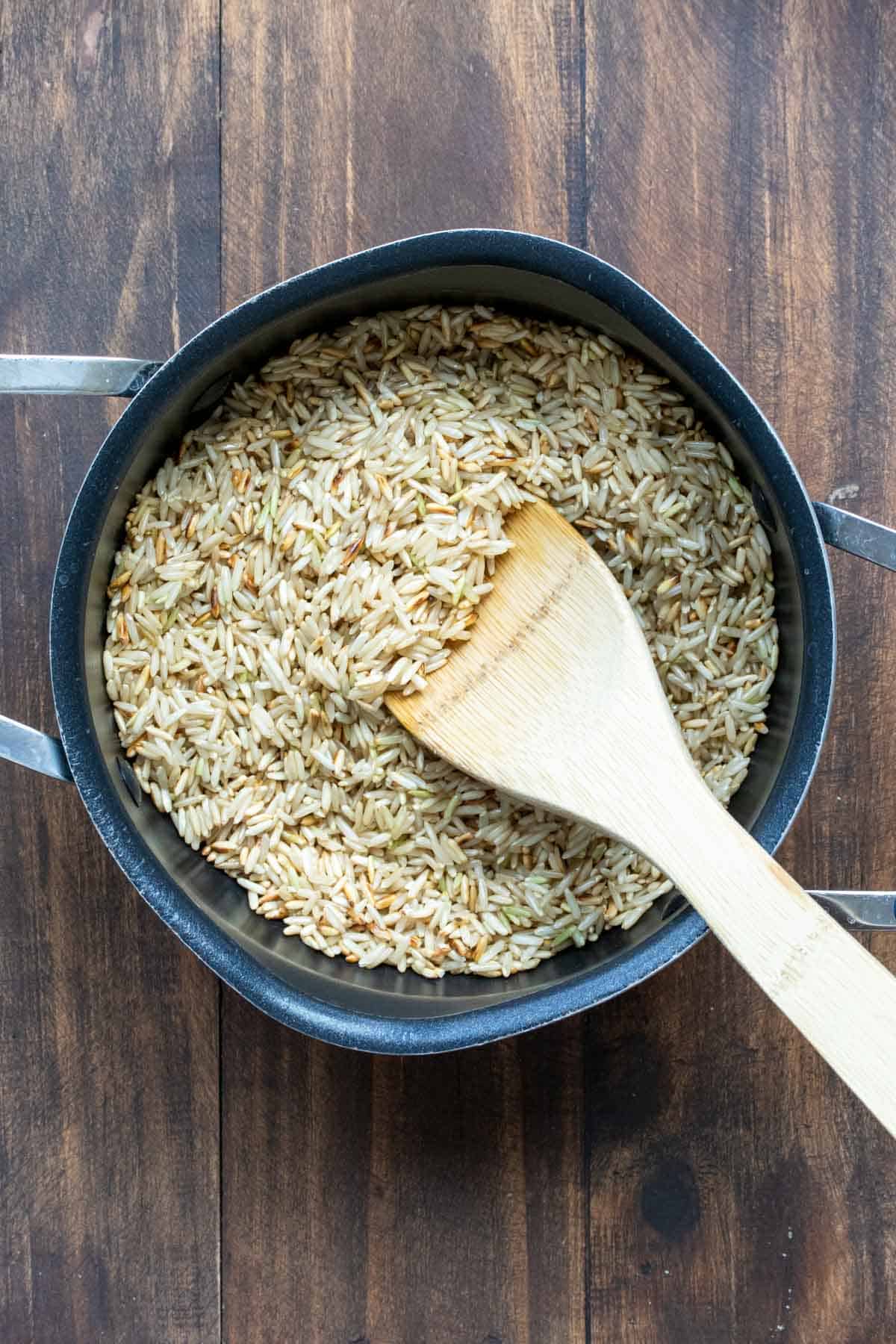 Wooden spoon mixing long grain brown rice in a pot