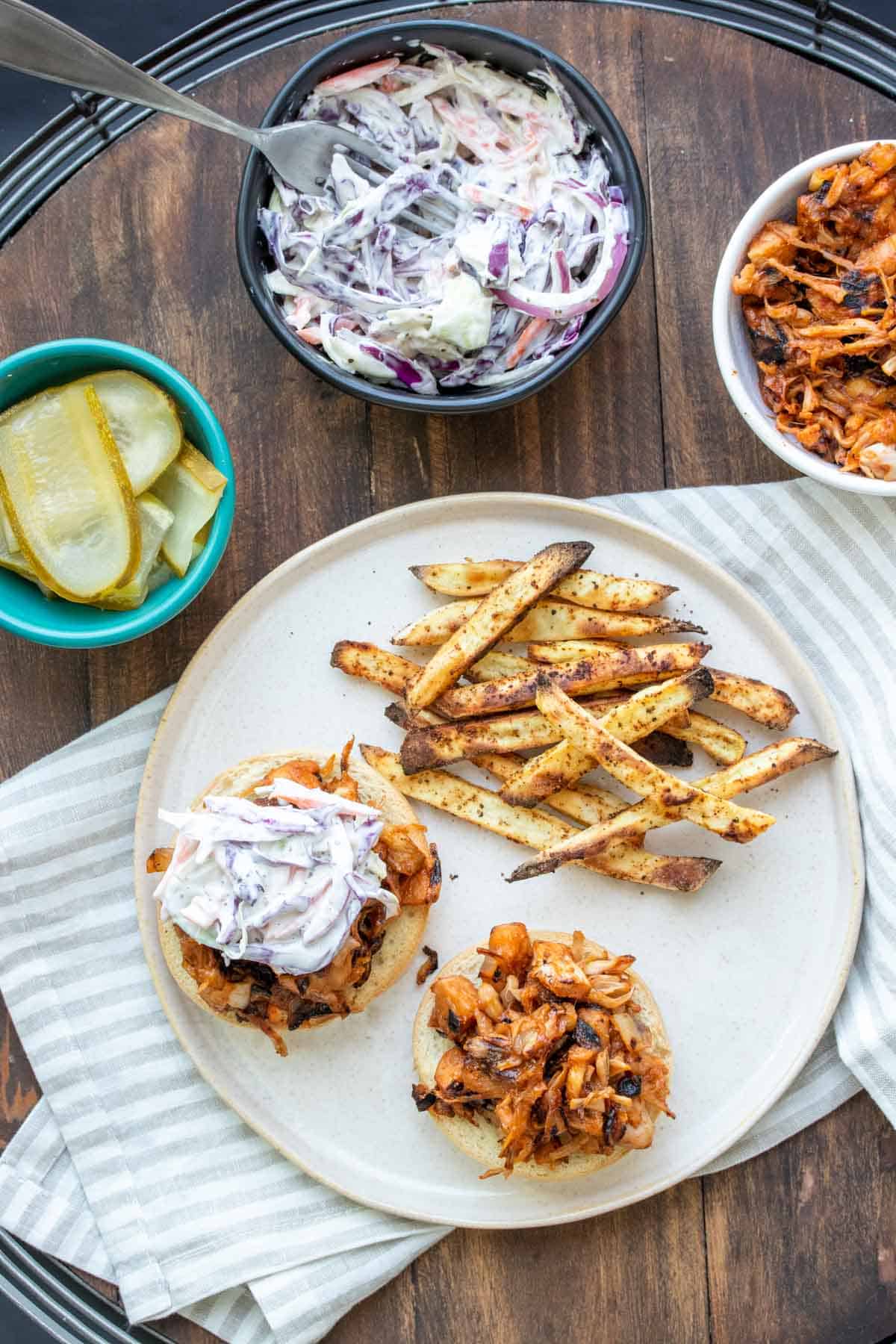 Top view of BBQ jackfruit sandwiches on a plate with coleslaw on top and next to fries.