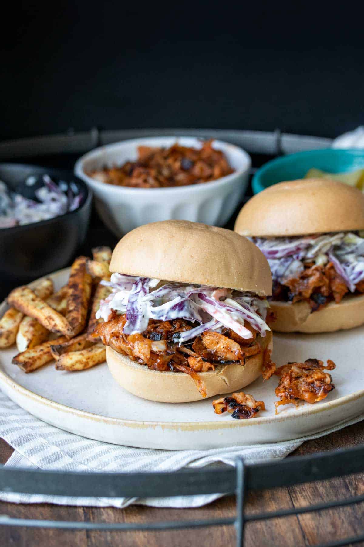 Side view of BBQ jackfruit topped with coleslaw on a bun sitting on a cream plate