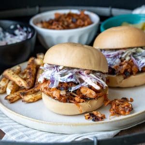 Cream plate with BBQ jackfruit sandwiches topped with coleslaw and fries.