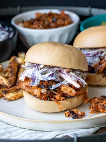 Cream plate with BBQ jackfruit sandwiches topped with coleslaw and fries.