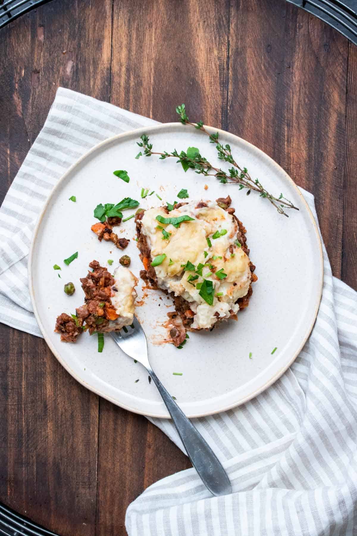 Top view of a piece of vegetarian Shepherd’s pie with a bite out of it on a white plate.