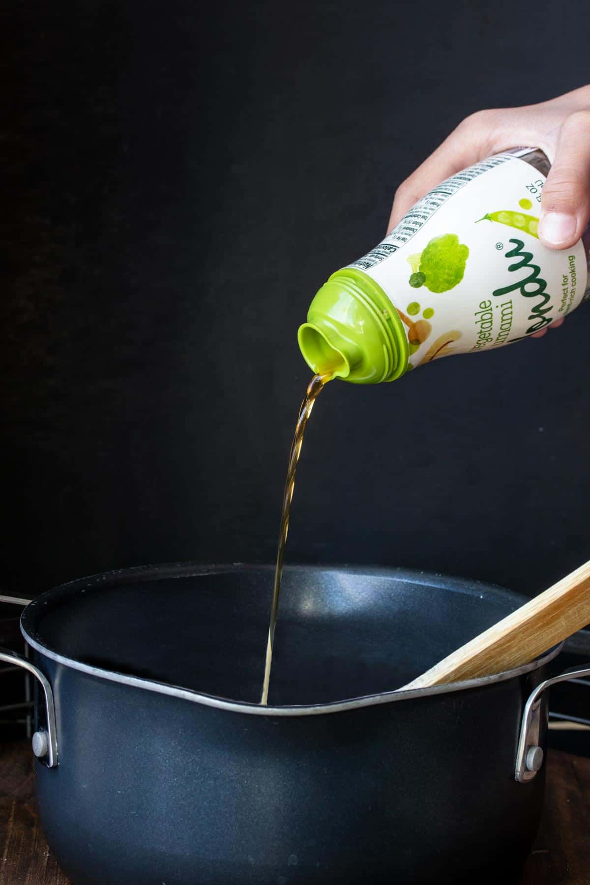 Hand pouring liquid out of a green and white container into a pot.