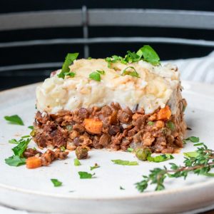 A white plate with a piece of cottage pie on it topped with parsley.