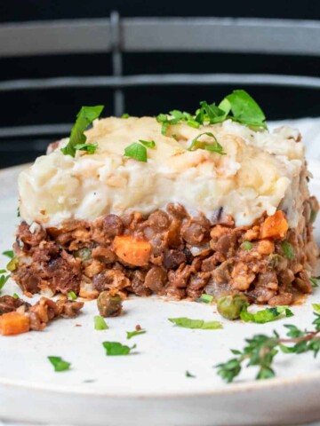 A white plate with a piece of cottage pie on it topped with parsley.