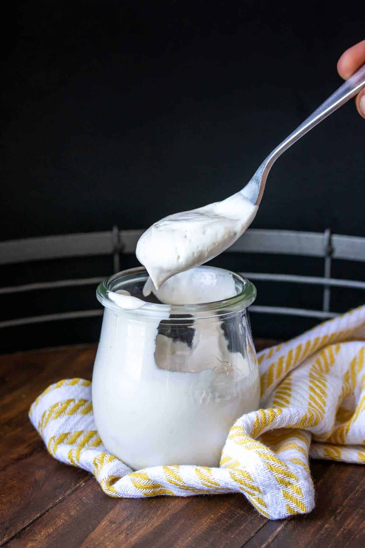 Spoon coming out of a glass jar with a scoop of sour cream on it