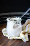 A jar filled with sour cream and a spoon in it sitting on a yellow striped towel.