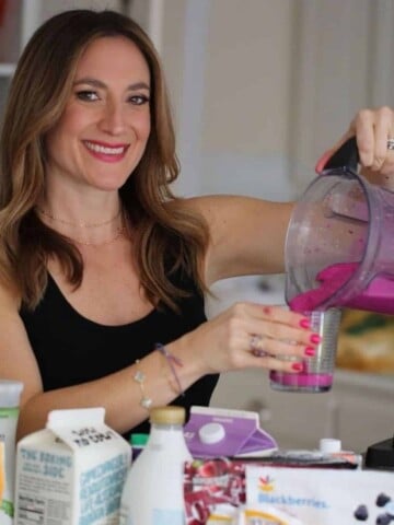 A lady pouring a hot pink smoothie into a cup surrounded by ingredients