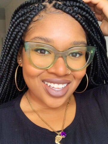 Photo of a black woman with glasses holding her hand on her head and smiling