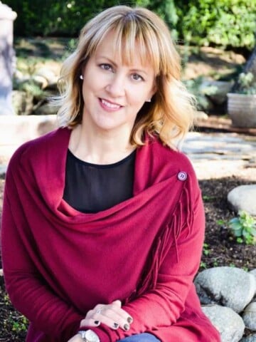 A woman with blond hair wearing a magenta sweater sitting on a rock wall