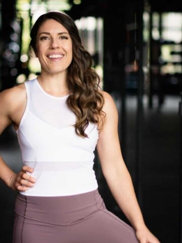 A woman with long brown hair standing in workout gear and hand on her hip