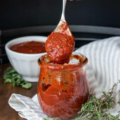 Hand using a spoon and grabbing a scoop of pizza sauce from a glass jar