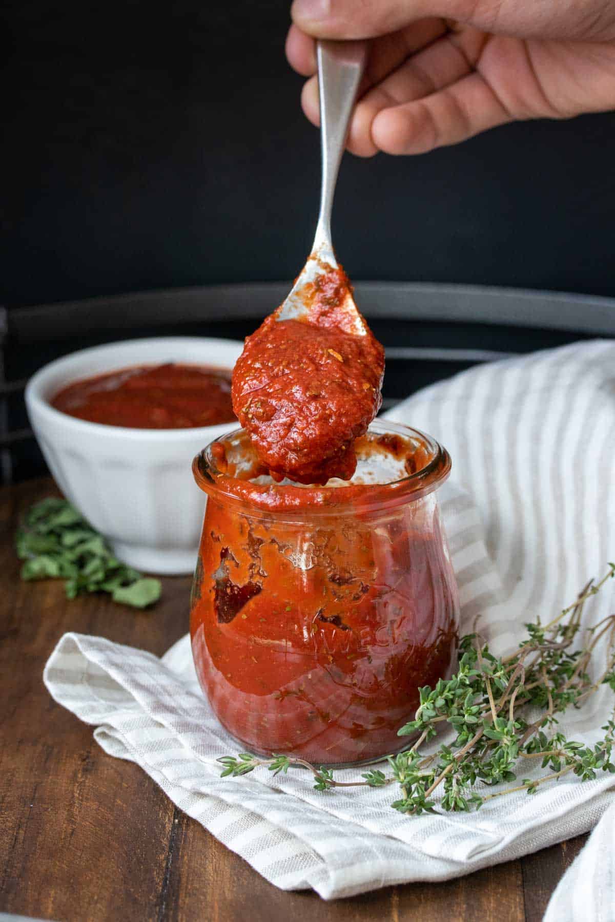 Hand using a spoon and grabbing a scoop of pizza sauce from a glass jar