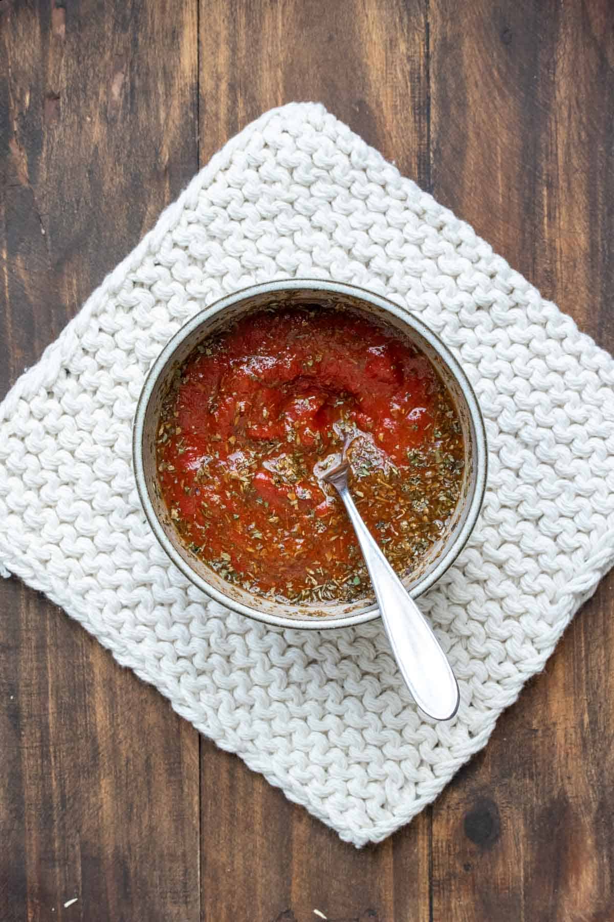 Top view of a bowl with a spoon mixing up a pizza sauce