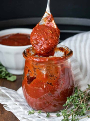 Spoon coming out of a jar of pizza sauce on a tan and white striped towel