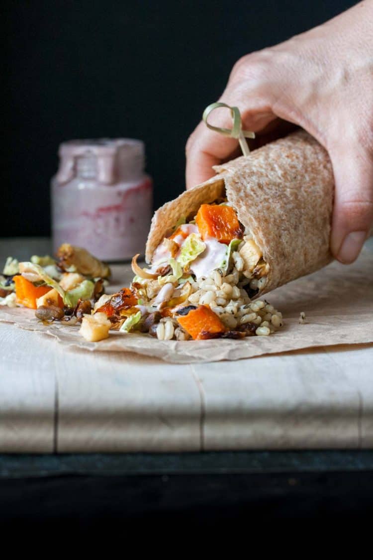 Hand holding a burrito with roasted veggies and rice coming out of the front