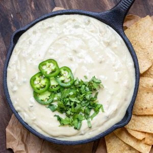 A black cast iron pan filled with white queso dip that is topped with sliced jalapenos and chopped cilantro.