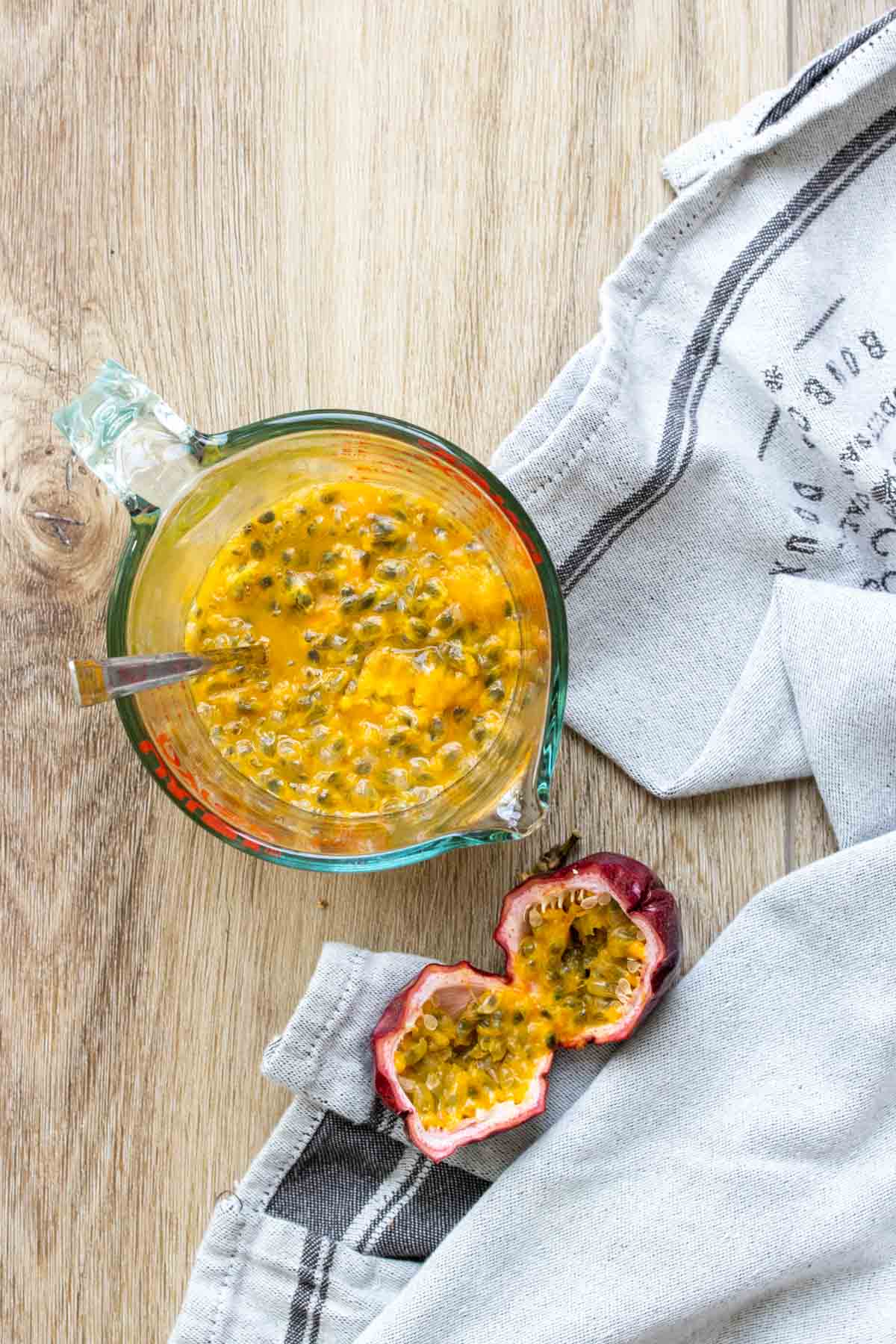 Top view of a glass measuring cup with passion fruit pulp inside next to an open fruit