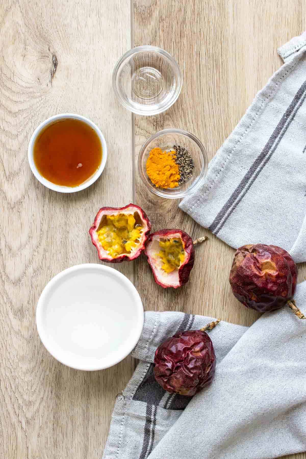 Overhead shot of cut open passion fruit, water, syrup and spices on a wooden surface
