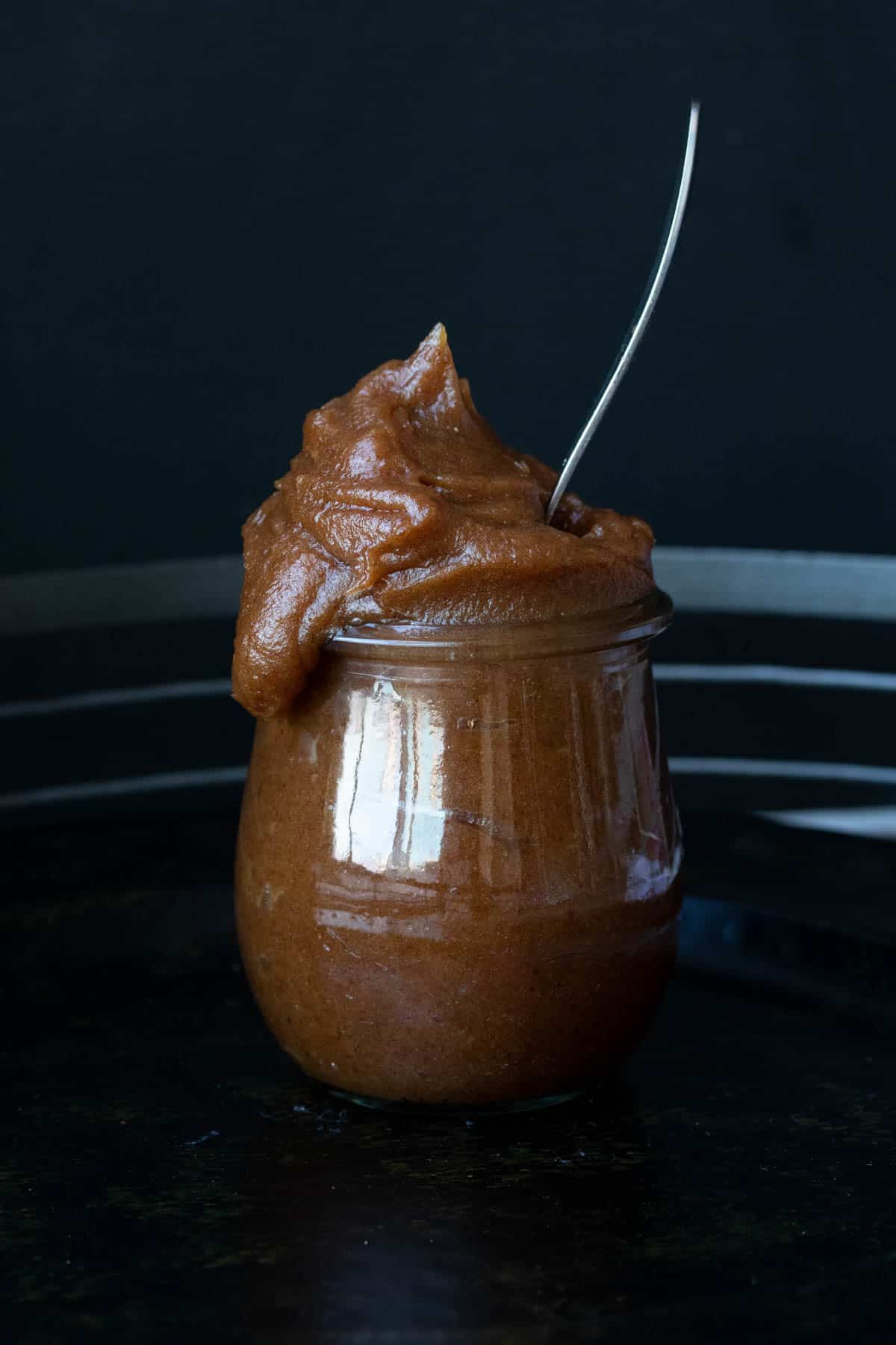 Date paste spilling out of the top of a glass jar with a spoon in it