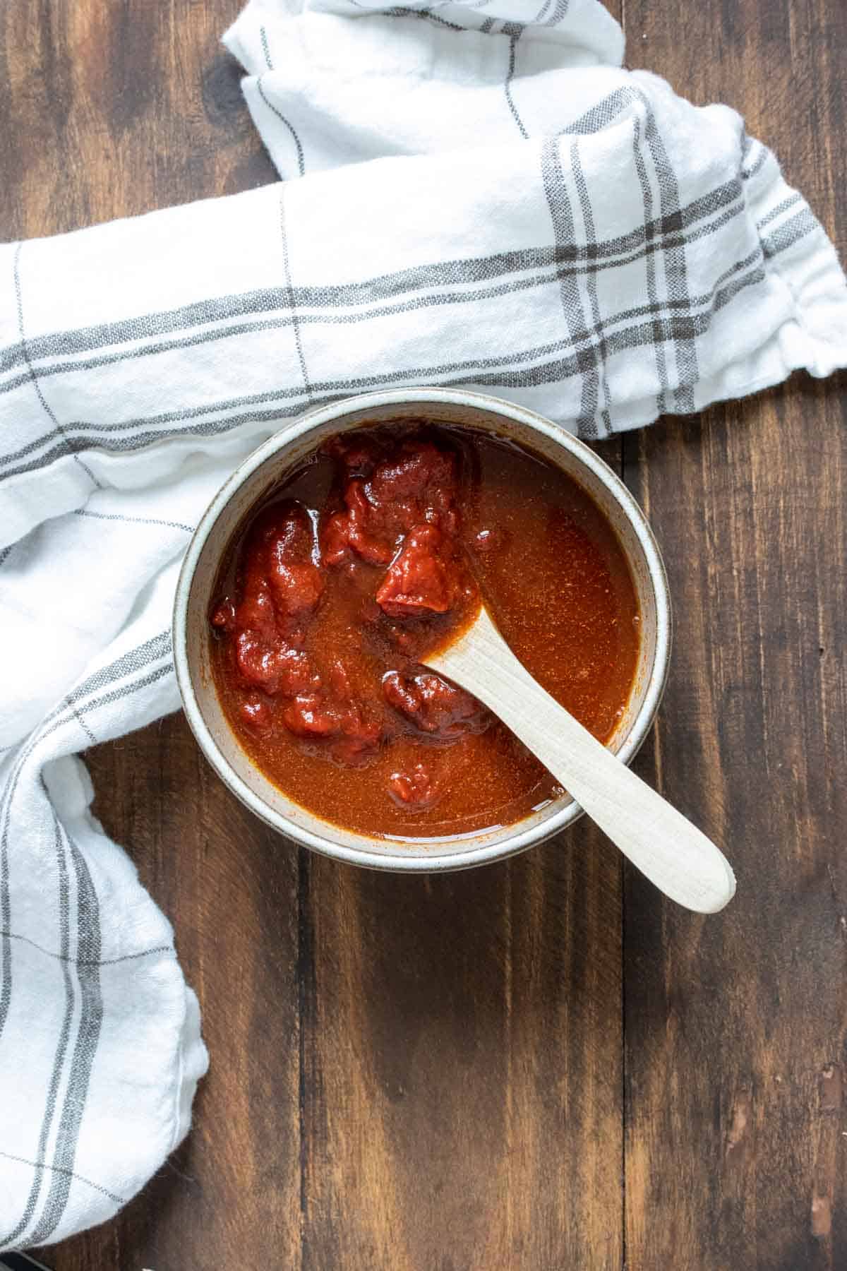 Wooden spoon mixing bbq sauce in a grey bowl