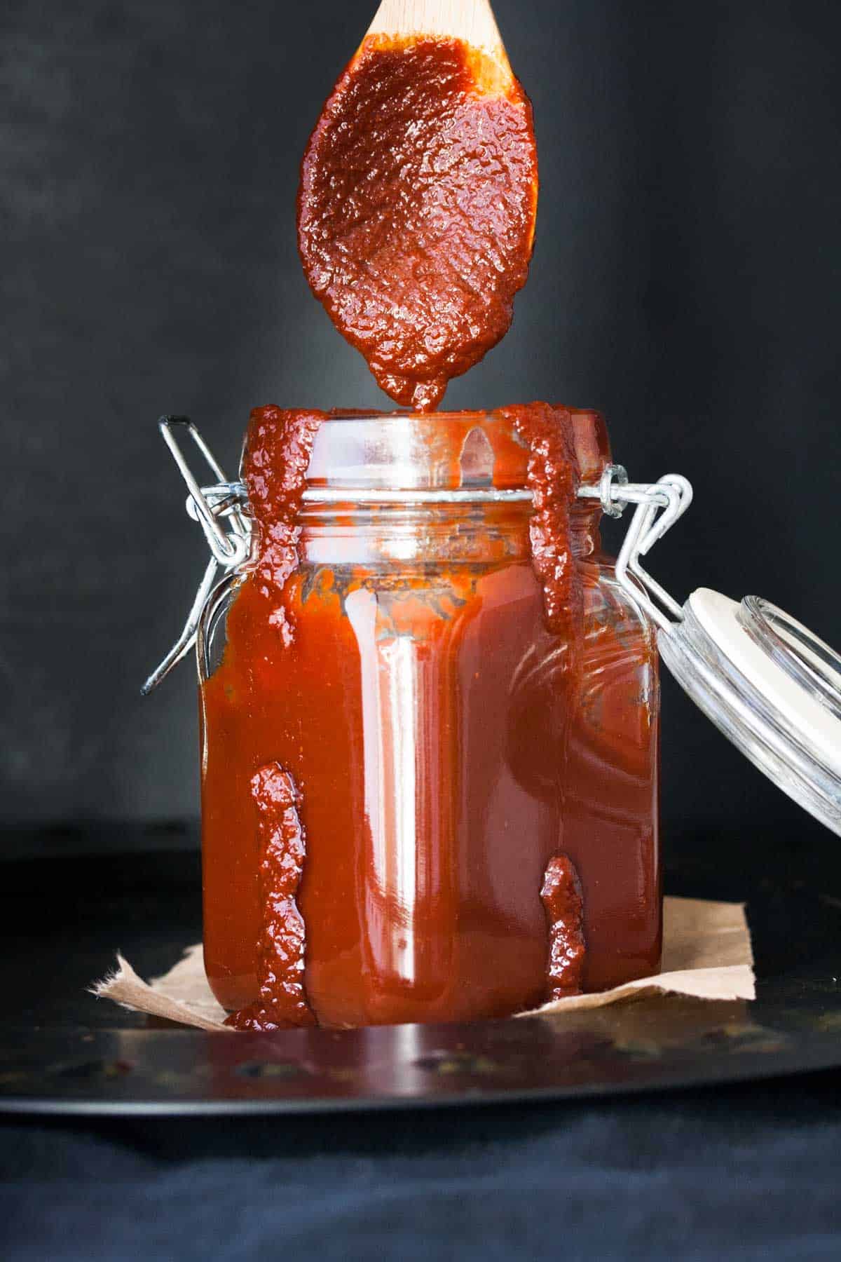 Spoon coming out of a glass storage jar filled with bbq sauce