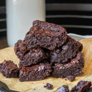 A pile of brownies on a piece of parchment paper with milk behind them