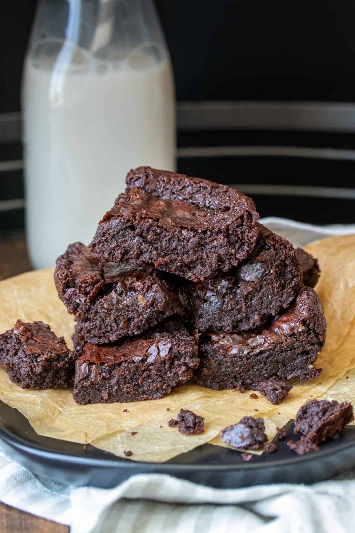 A pile of brownies on a piece of parchment paper with milk behind them