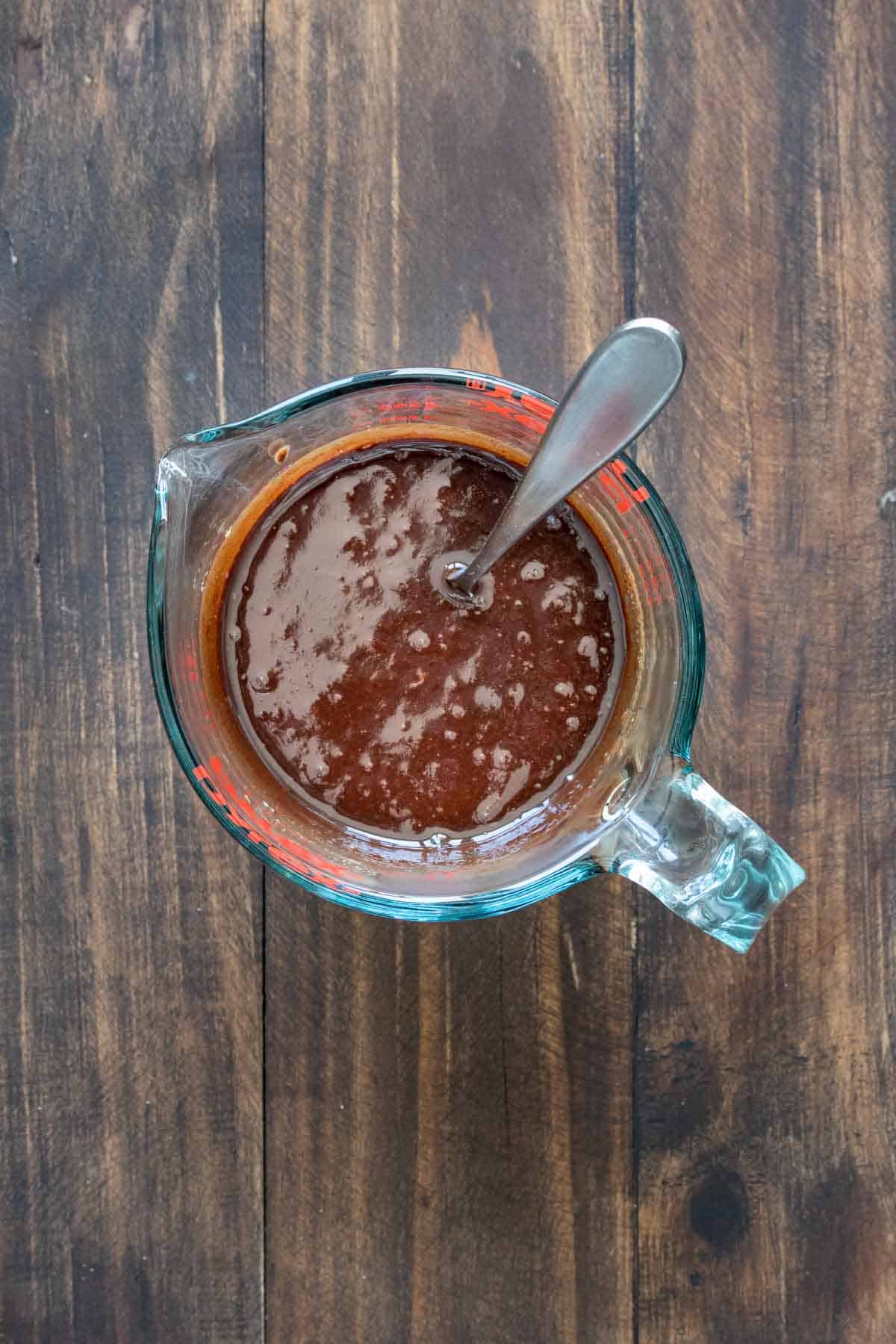 Top view of a glass measuring cup with melted chocolate and a spoon inside