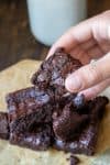 Hand holding a brownie with a bite out of it in front of a pile of more