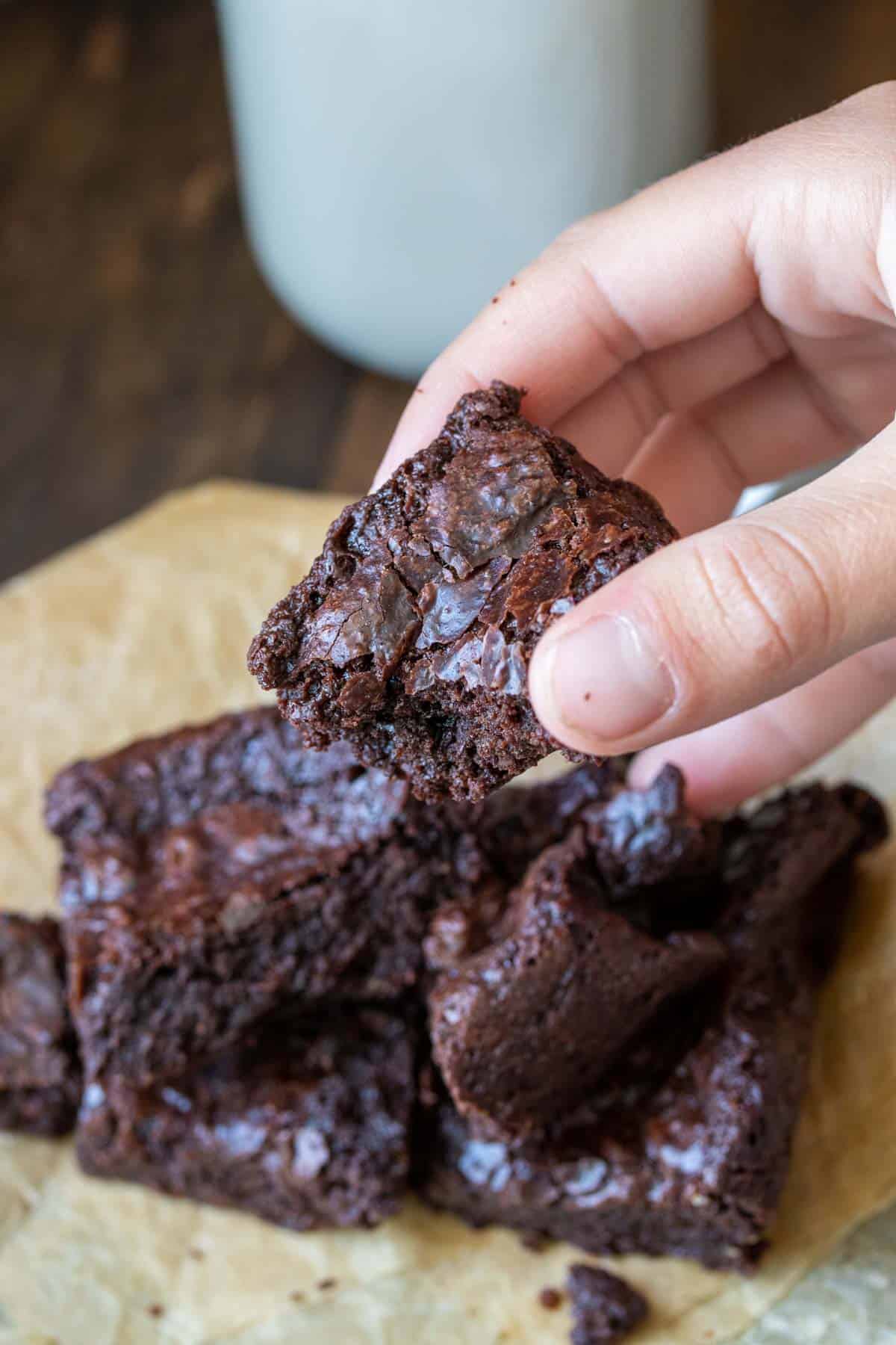 Hand holding a brownie with a bite out of it in front of a pile of more.