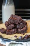 A pile of brownies on a piece of parchment on a black plate sitting on a striped blue towel.