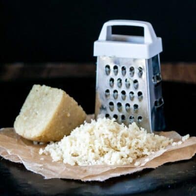 A pile of grated Parmesan next to a grater and a piece of the cheese block