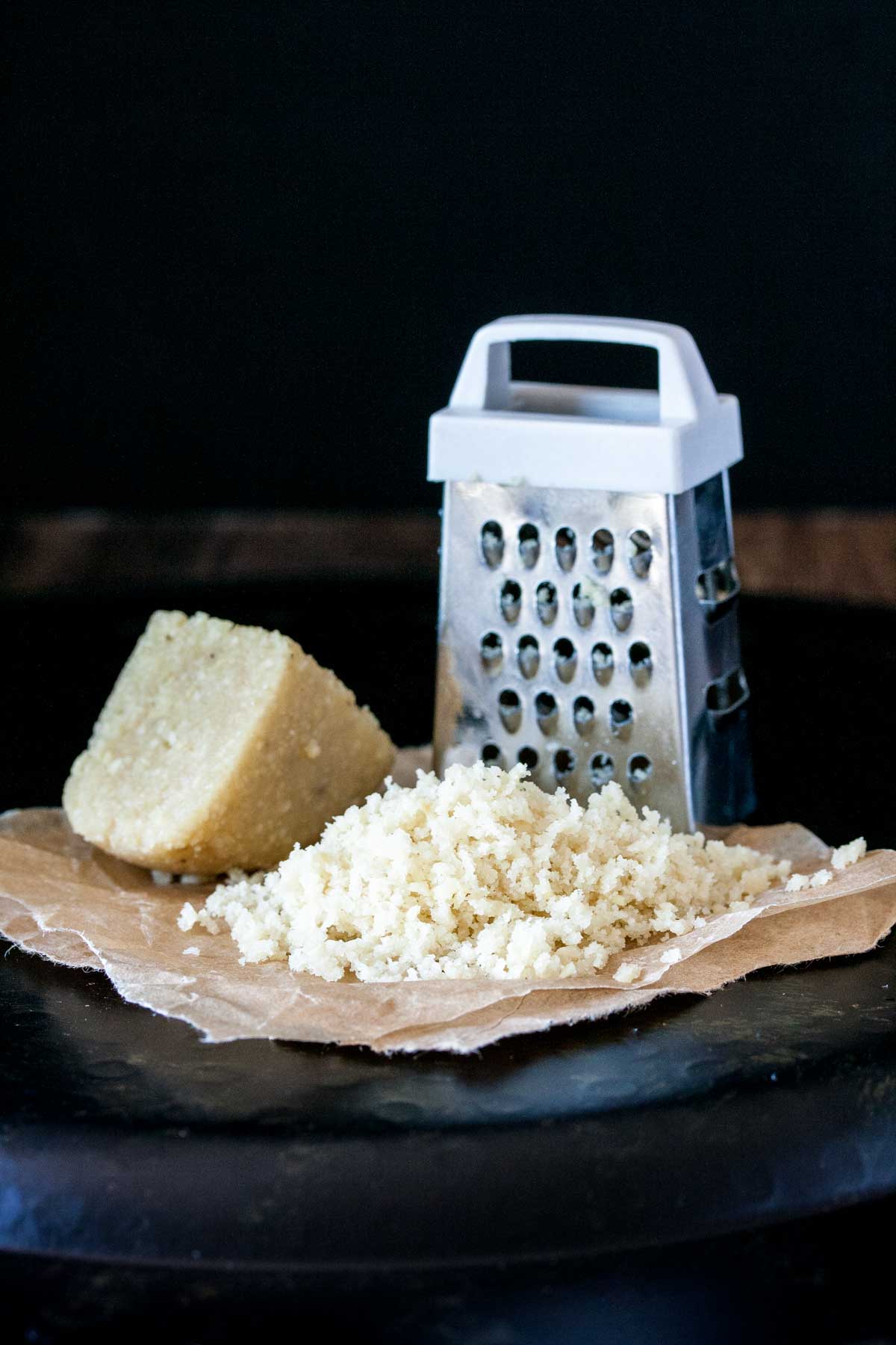 A pile of grated Parmesan next to a grater and a piece of the cheese block.