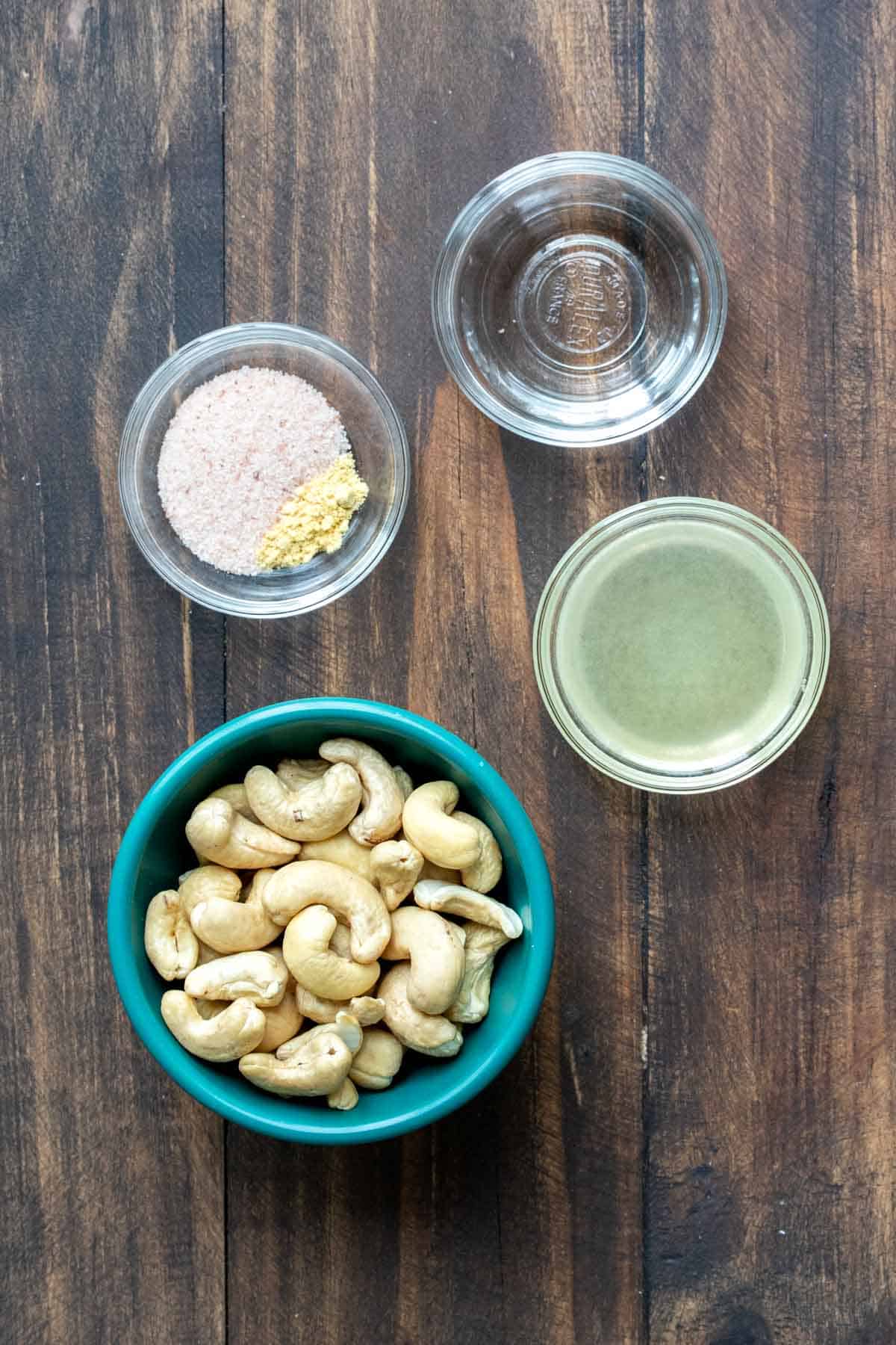 A bowl of cashews, salt, lemon juice and white vinegar on a wooden surface