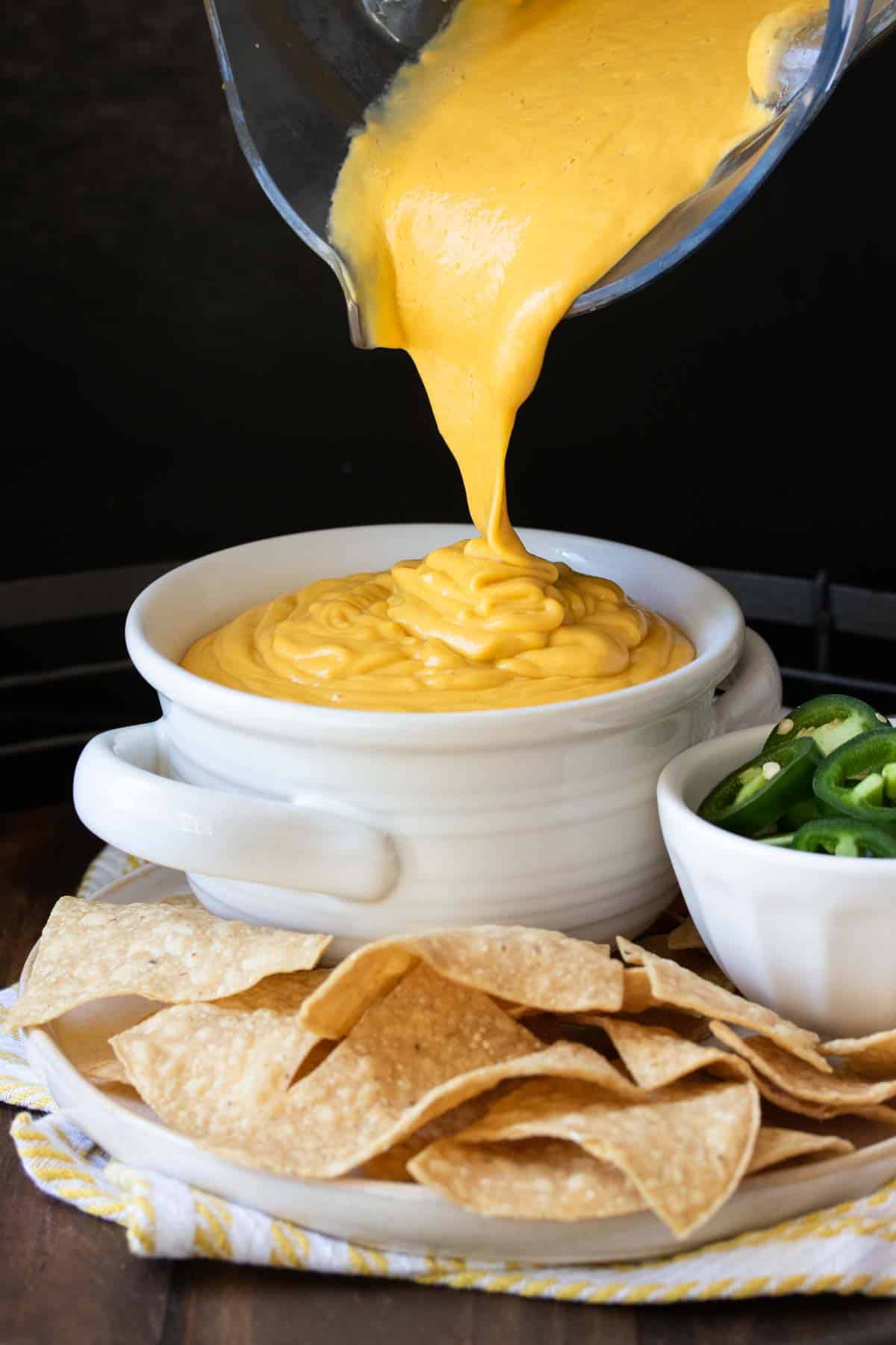 Cheese sauce being poured into a white soup bowl.