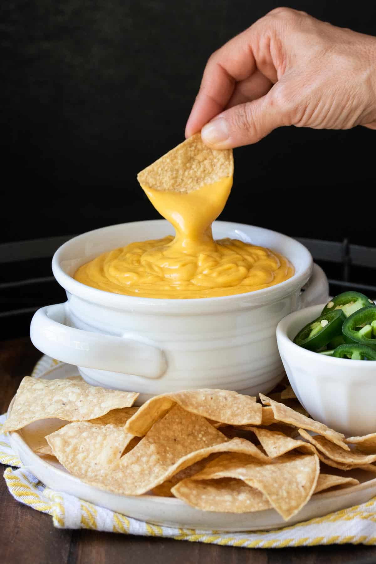 Hand dipping a chip in a bowl of orange cheese sauce