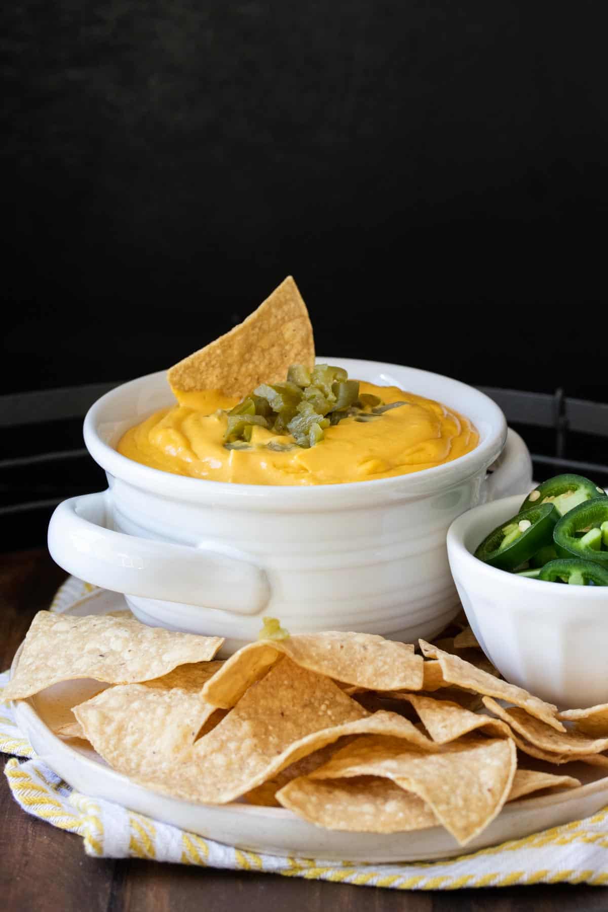White bowl filled with cheese sauce and chopped chiles and a chip on top.