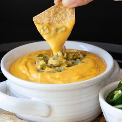 Hand dipping a tortilla chip into a bowl of cheese sauce
