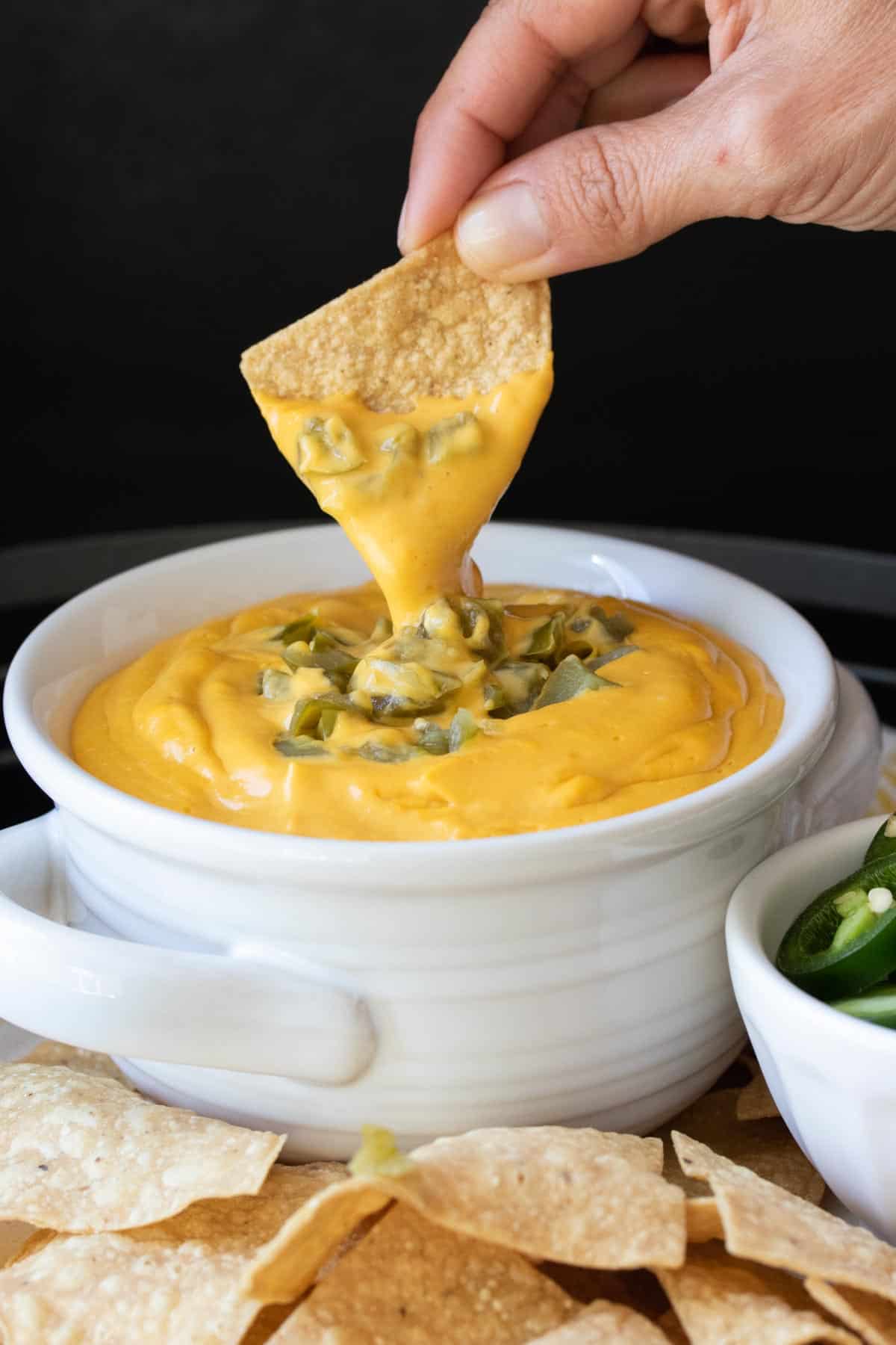 Hand dipping a tortilla chip into a bowl of cheese sauce.