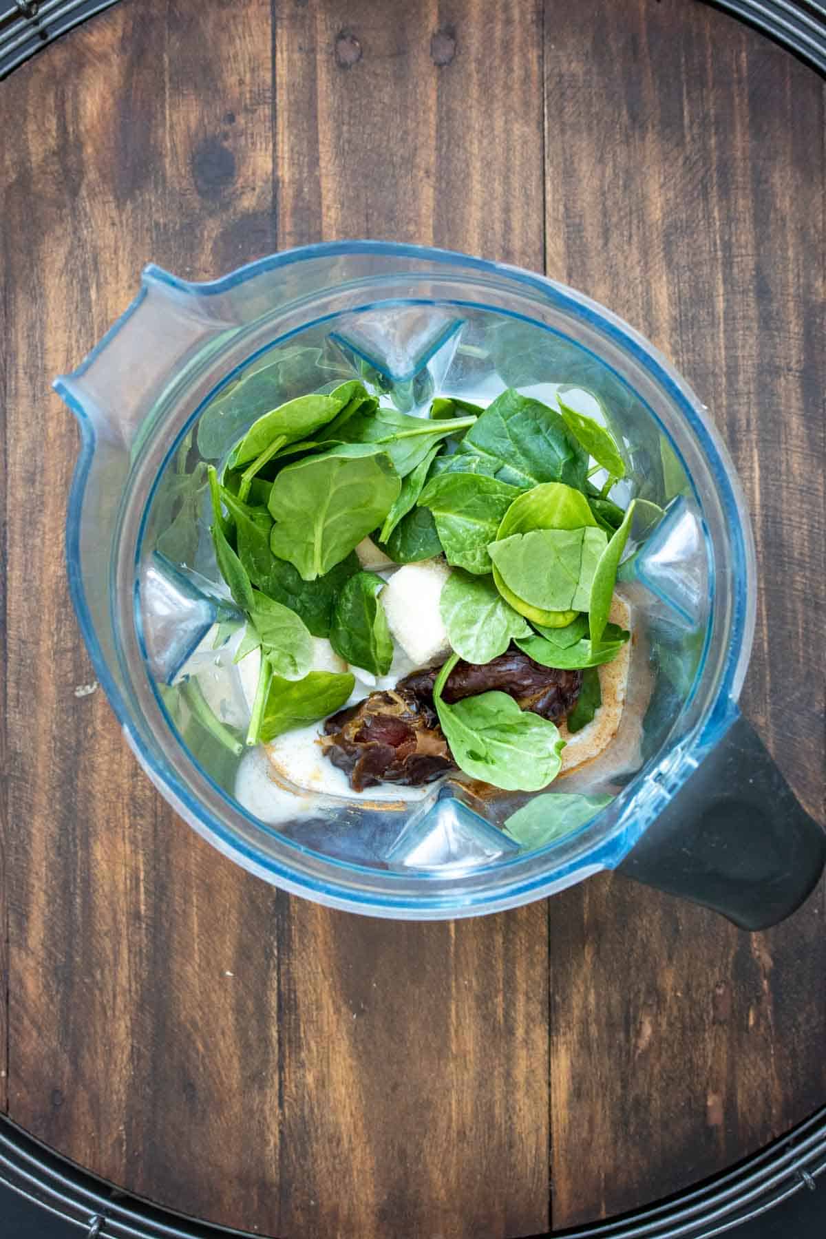 Top view of a blender with ingredients inside to make a spinach banana smoothie