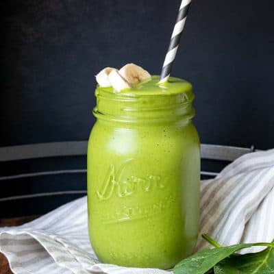 A green smoothie with sliced bananas on the top in a glass jar