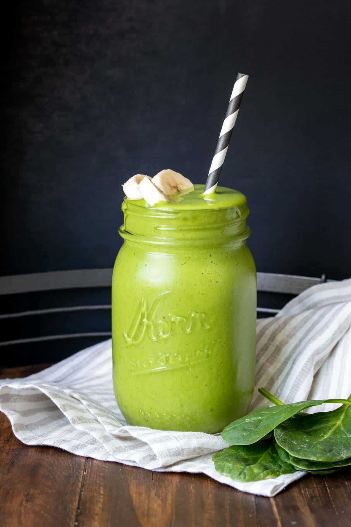 A green smoothie with sliced bananas on the top in a glass jar