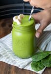 Boy holding a glass jar with a green smoothie and sipping it from a straw