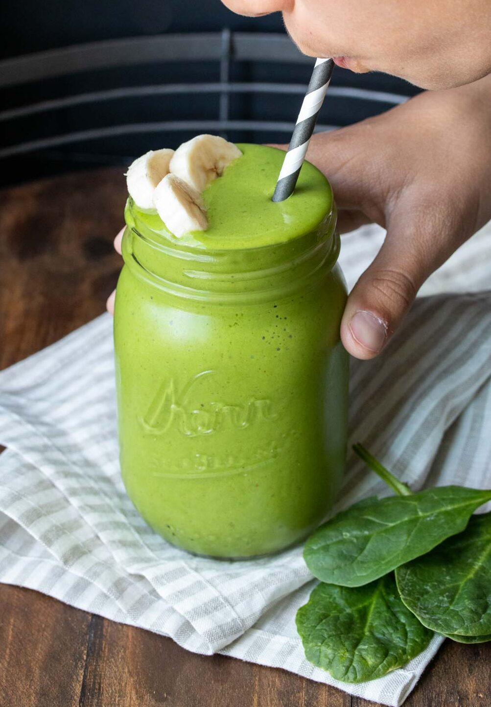 Boy holding a glass jar with a green smoothie and sipping it from a straw