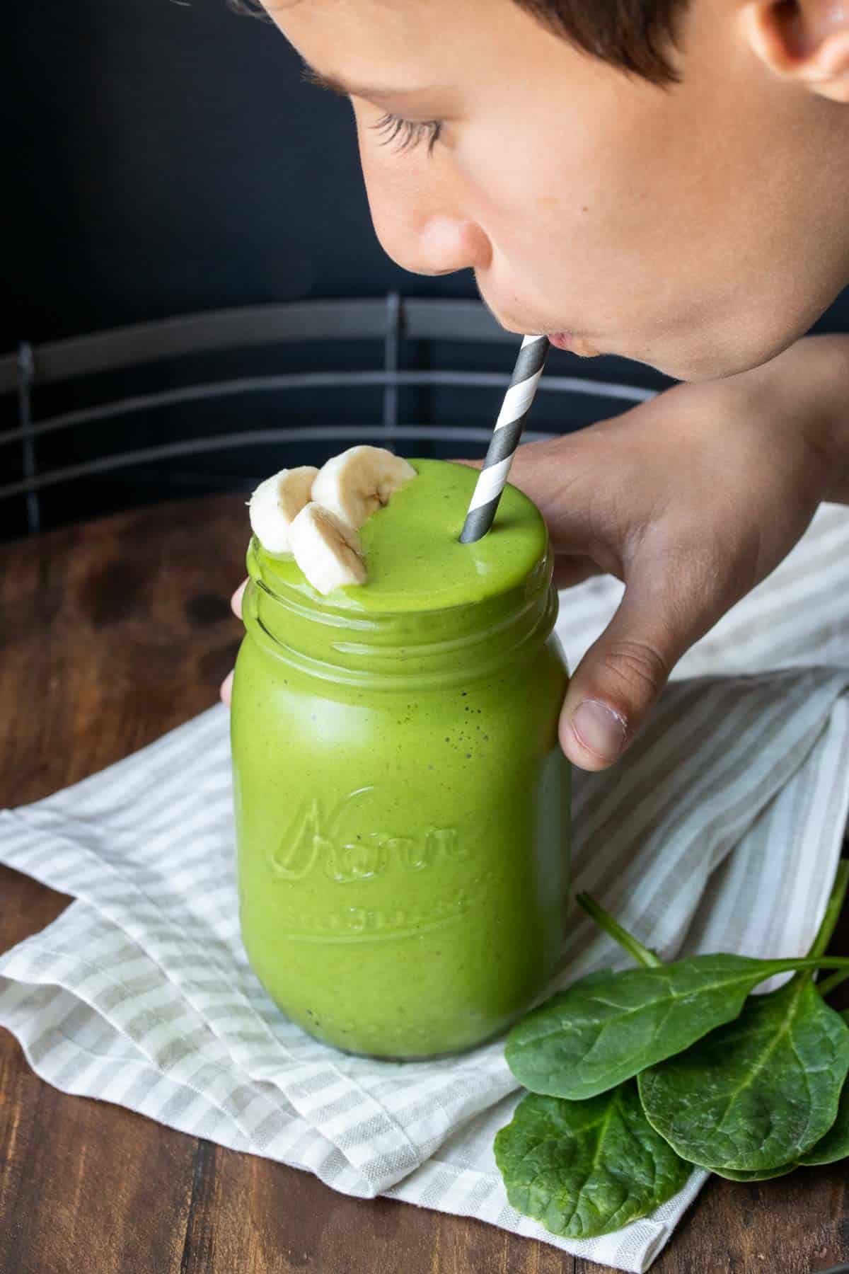 Boy holding a glass jar with a green smoothie and sipping it from a straw