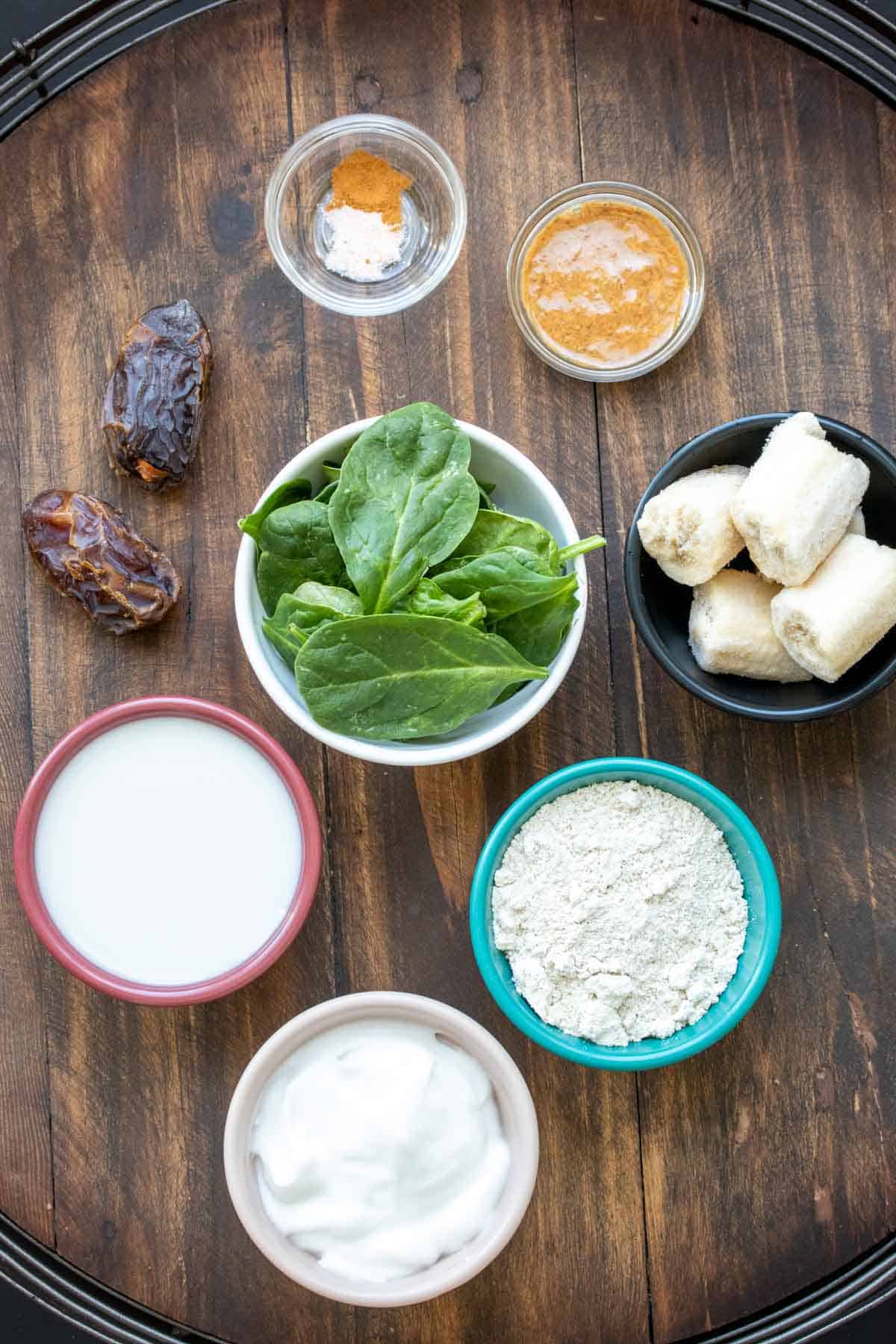 Different colored bowls filled with ingredients to make a spinach banana smoothie